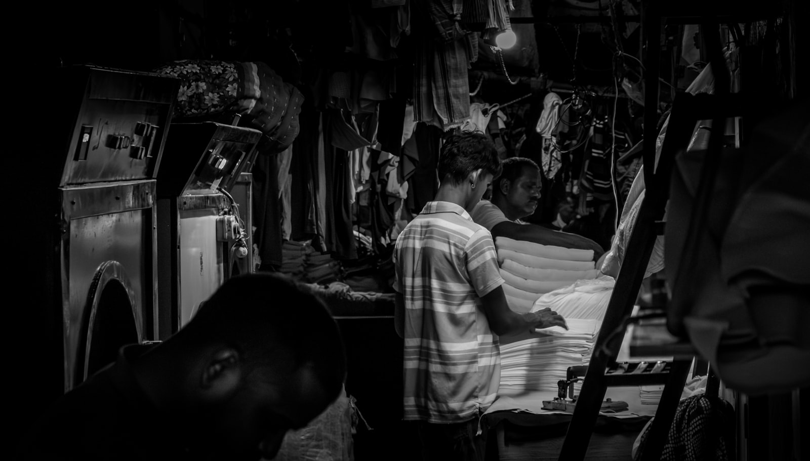 A presser folding garments alone in the dim workroom after hours