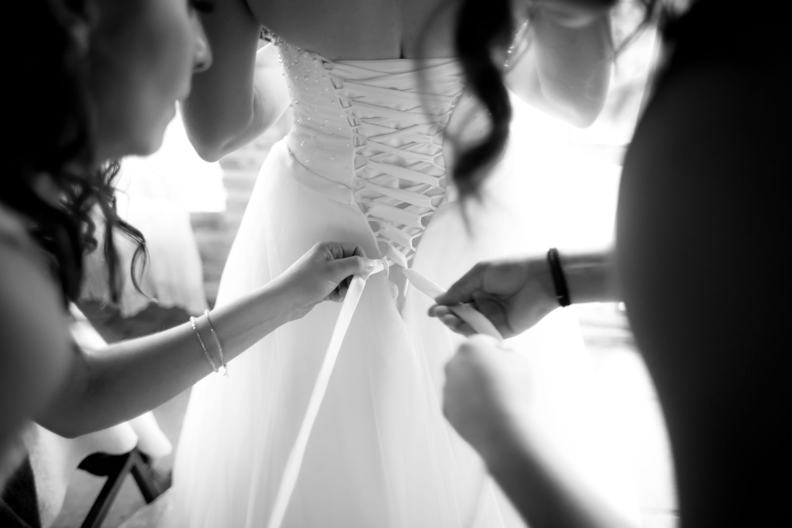 Hands lacing the back of a wedding gown, photographed in black and white